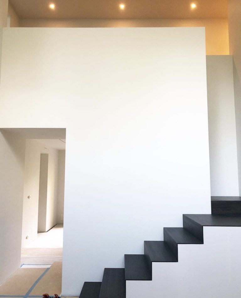 Modern och stilren interiör av ett 60-talshus i Stockholm med vita väggar och svarta trappsteg, upplyst av diskret takbelysning, ett exempel på en nöjd referenskund som fått professionell belysningskonsultation.